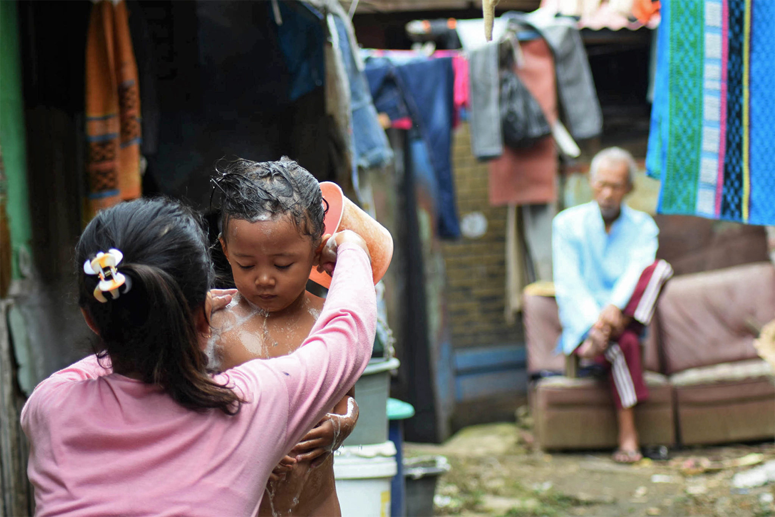 A woman bathes her younger sister with water from a reservoir 