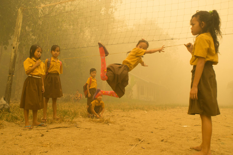 Children play without wearing any protection at a playground in thick haze.