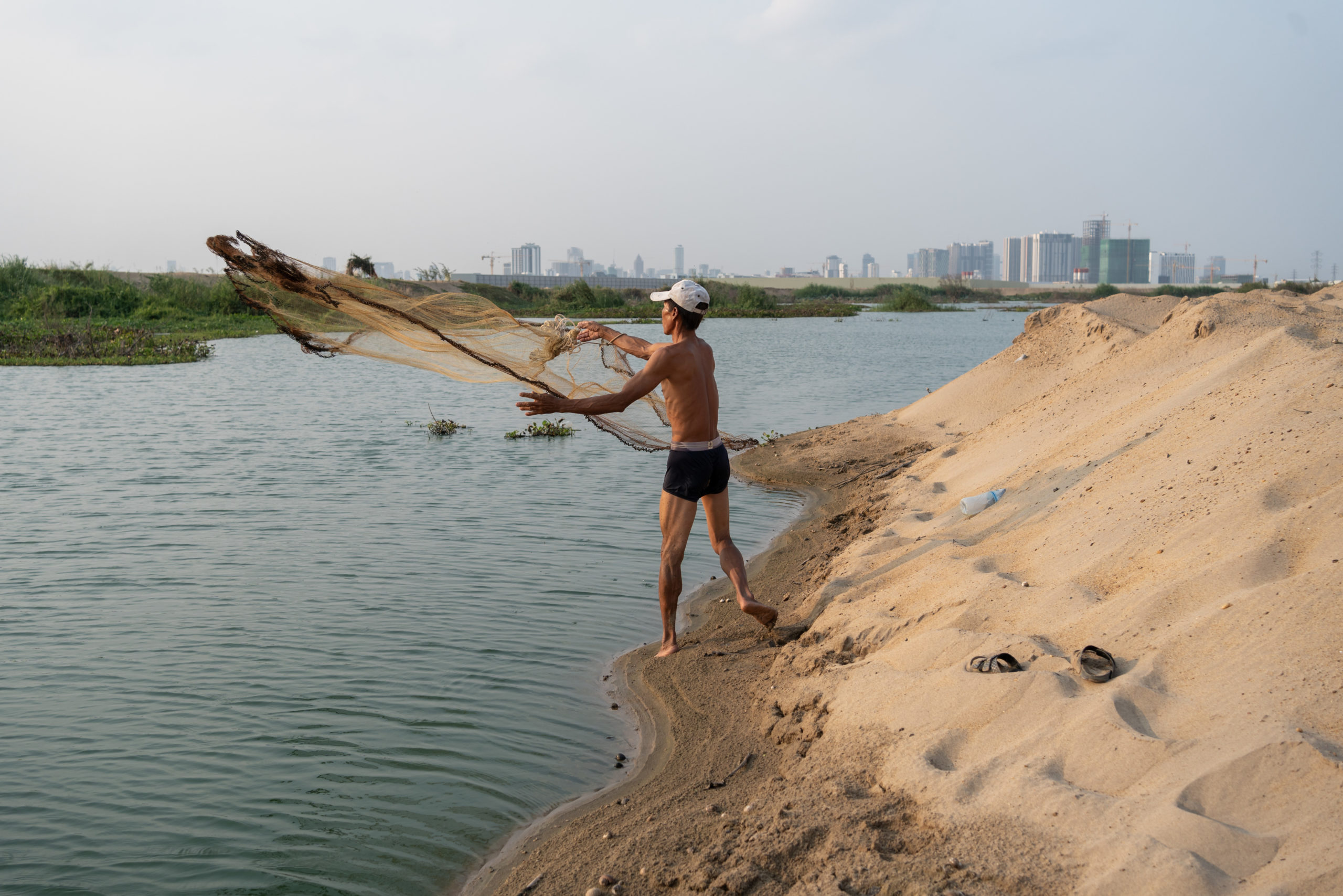 A man attempts to fish in what remains of Boeung Tompoun