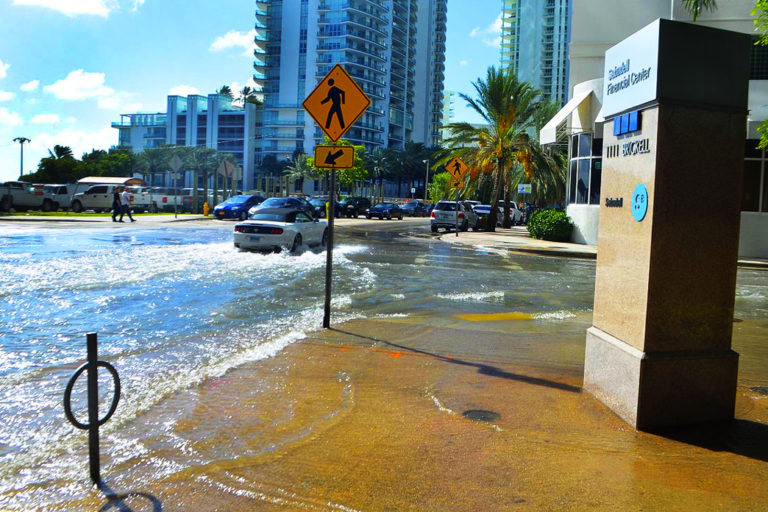 High tide flooding in downtown Miami. The useful life of roads and other infrastructure is shortened dramatically by repeated saltwater inundation. Image via Wikimedia Commons.