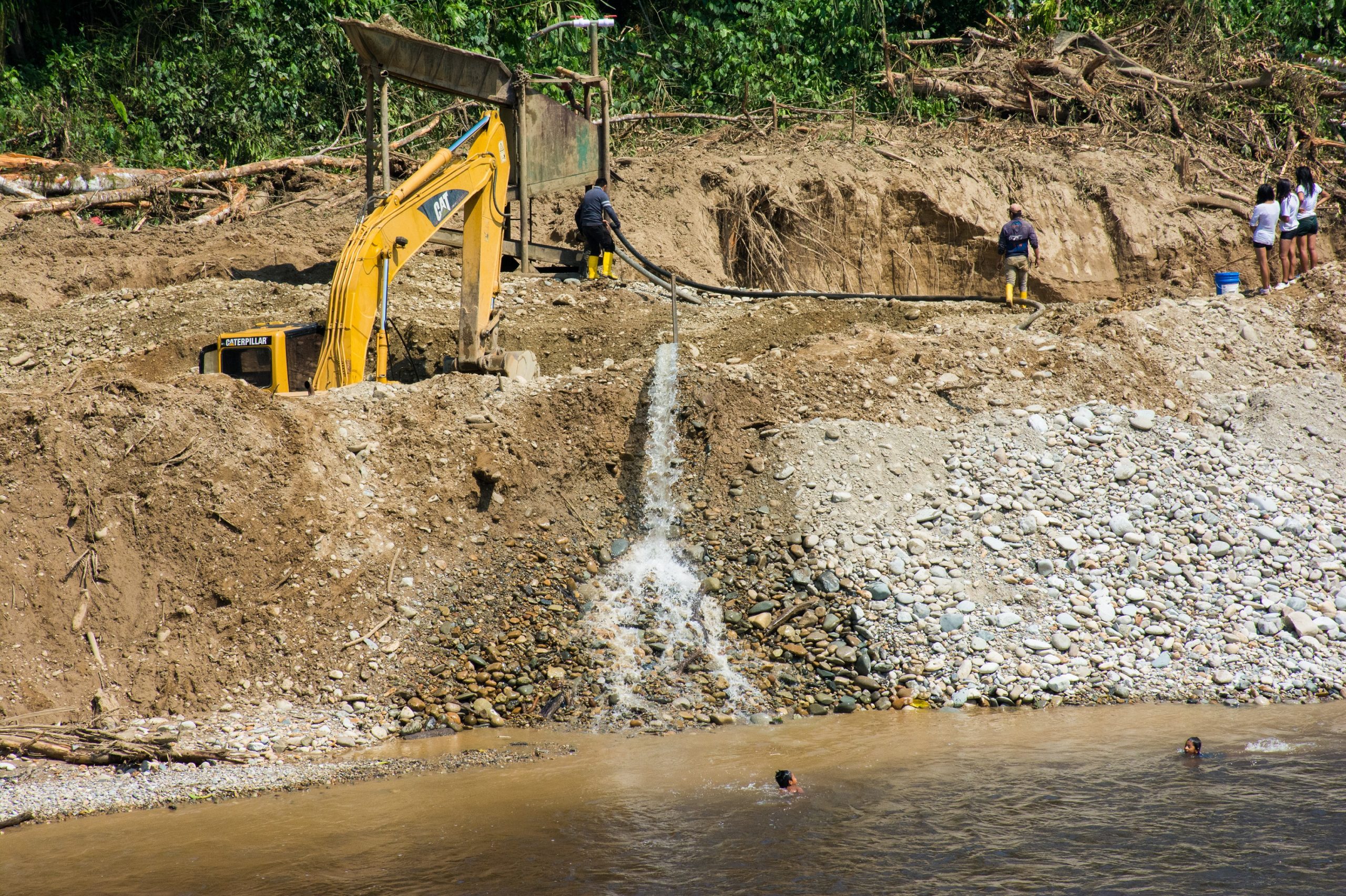 Two children play in the upper basin of the Nangaritza River, while a group of miners extract gold in the Shaime community. Photo taken in 2018 by Carlos Medina.